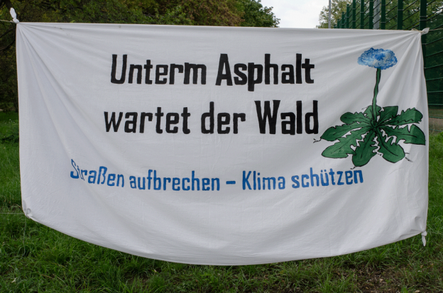 Banner mit der Aufschrift "Unterm Asphalt wartet der Wald - Straßen aufbrechen - Klima schützen"